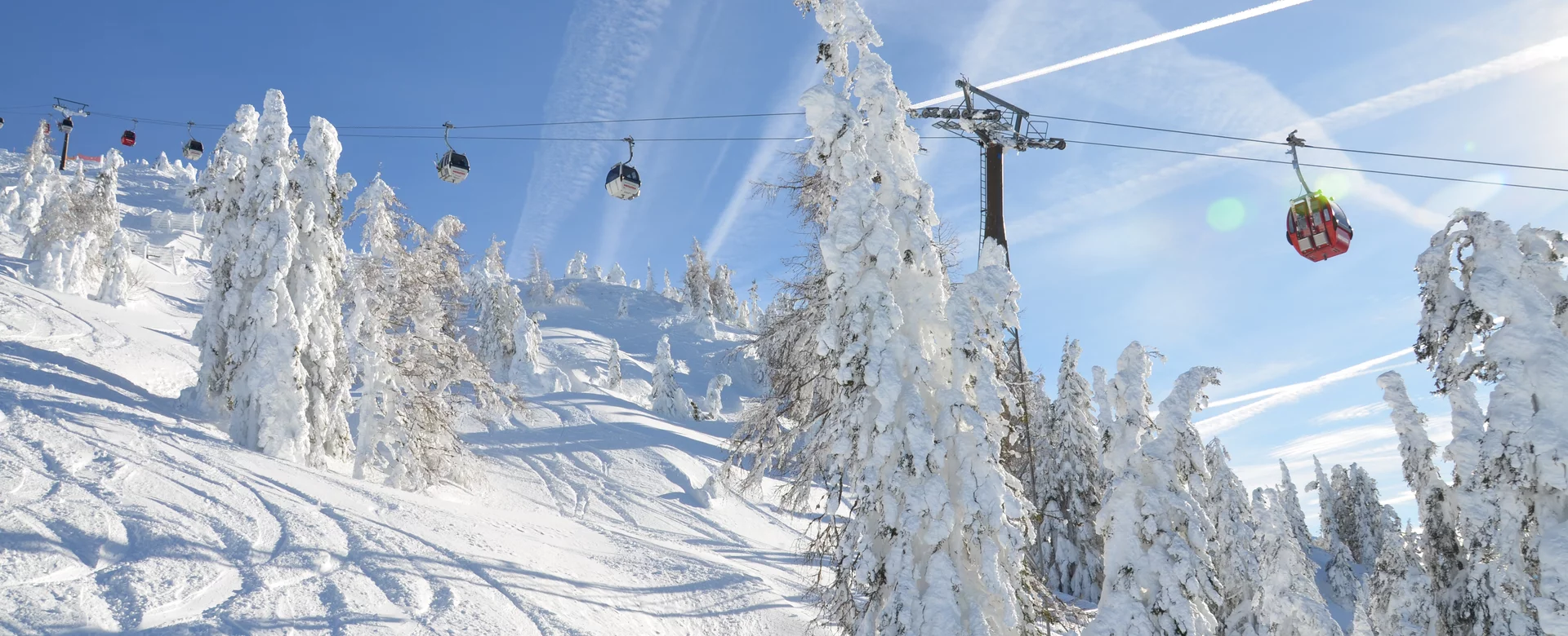 Snedækkede træer under en klar blå himmel i Saalbach, med en skilift, der løber over scenen. Jorden er dækket af sne og viser skispor. Solen skinner kraftigt, hvilket skaber linseudstråling, og kontrasider er synlige over hovedet.