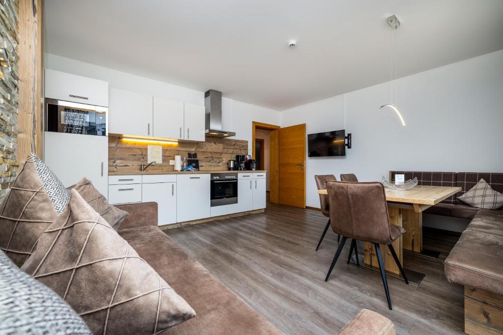 Moderne køkken og spiseplads med hvide skabe, træbordplader og vægge med stenaccent. En U-formet sofa og spisebord med brune stole sidder på trægulv. Vægmonteret tv og ovenlys fuldender den hyggelige opsætning.