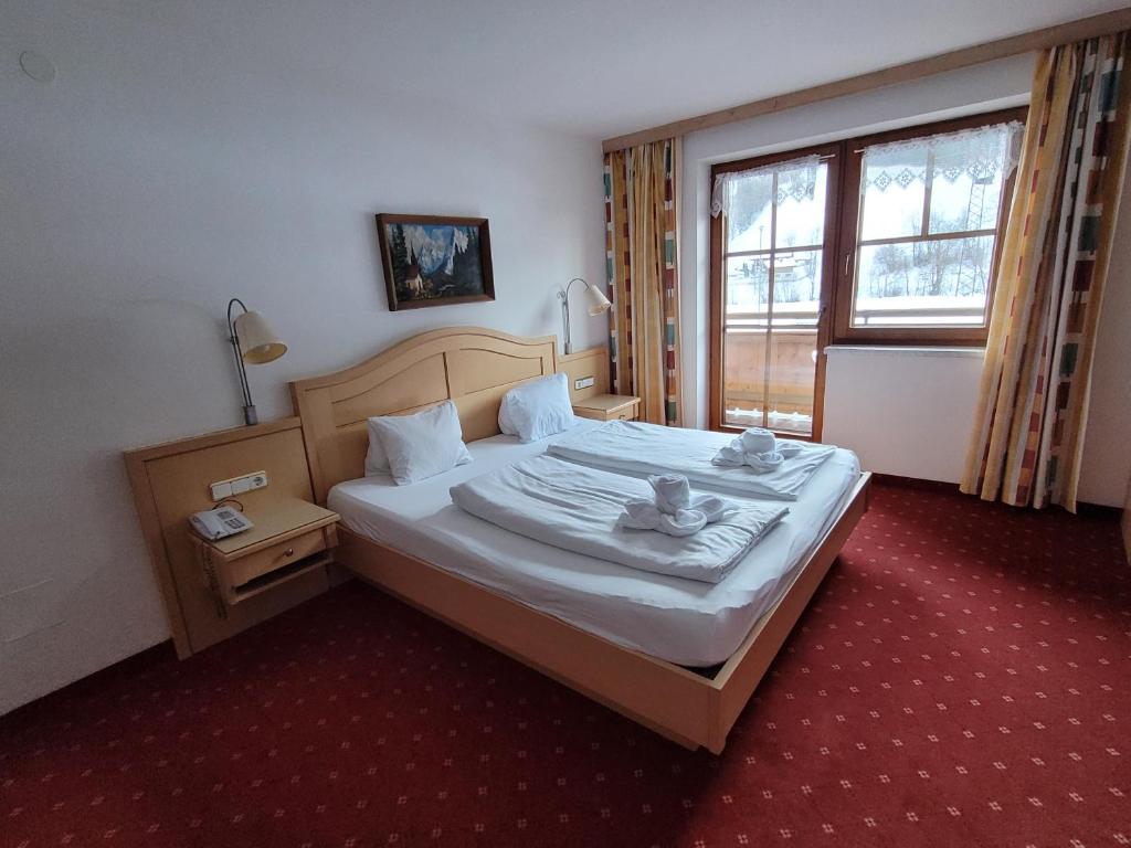 Hotelværelse med en stor seng dækket af hvidt sengetøj og puder. Væggene er lyse med et landskabsbillede over sengen. To sengelamper og et bord med telefon er synlige. Et vindue med gardiner viser en sneklædt udendørs udsigt.