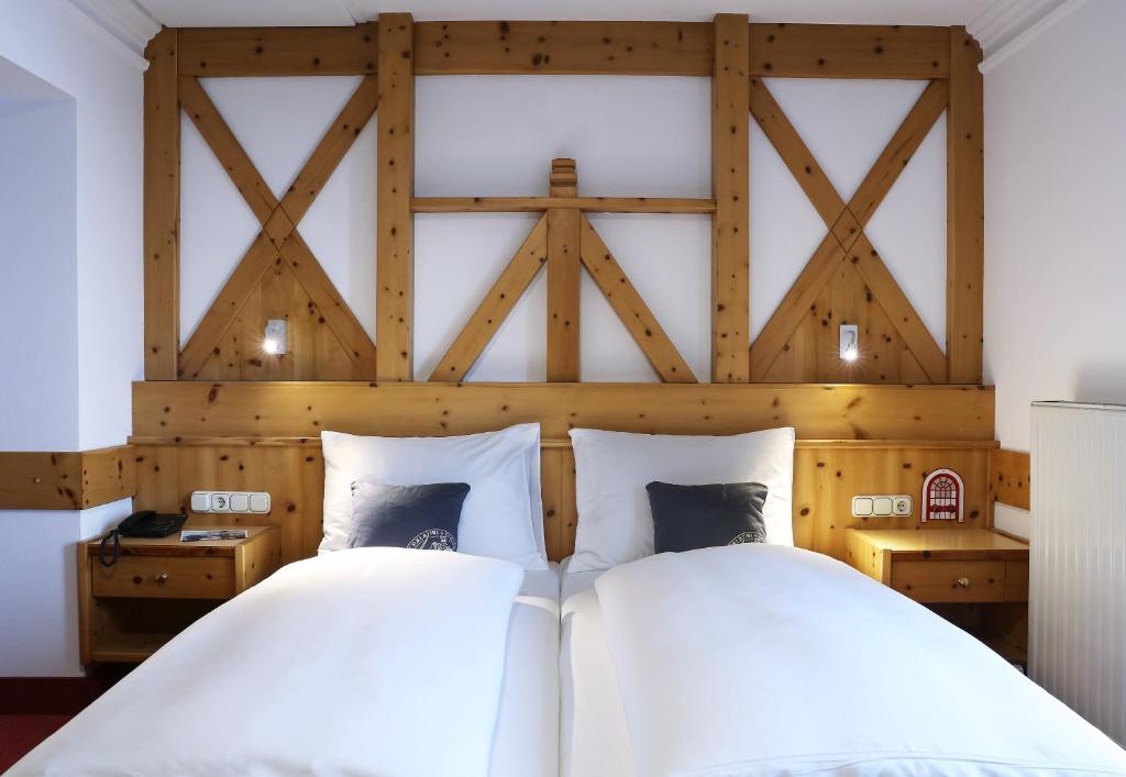 Et hyggeligt hotelværelse med to enkeltsenge skubbet sammen, hvidt sengetøj, sengegavl i træ med geometrisk design, natborde på hver side og væghængte læselamper over sengene.