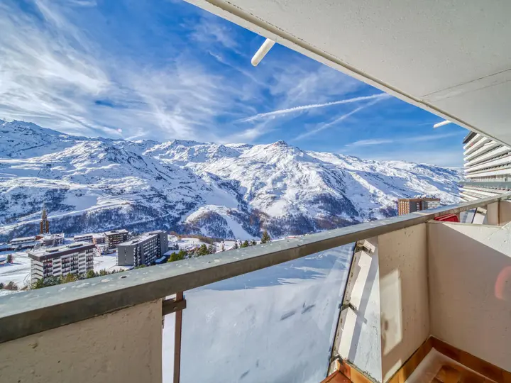 Udsigt fra en balkon med udsigt over en sneklædt bjergkæde under en klar blå himmel med tjusede skyer. Nedenfor er der bygninger beliggende i sneen, som viser et fredfyldt vinterlandskab.