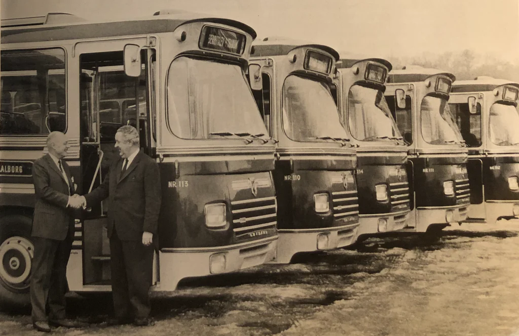 Thinggaard køber nye busser i 1970, to mænd giver hånd foran nye busser.