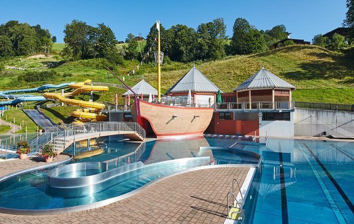 Oplev et stænk af sjov under din Sommerferie i Saalbach på vores udendørs svømmeområde, med en stor pool, skibstema legestruktur og farverige vandrutsjebaner. Omgivet af frodige grønne områder og træer under en klar blå himmel, er det den perfekte sommerferie.