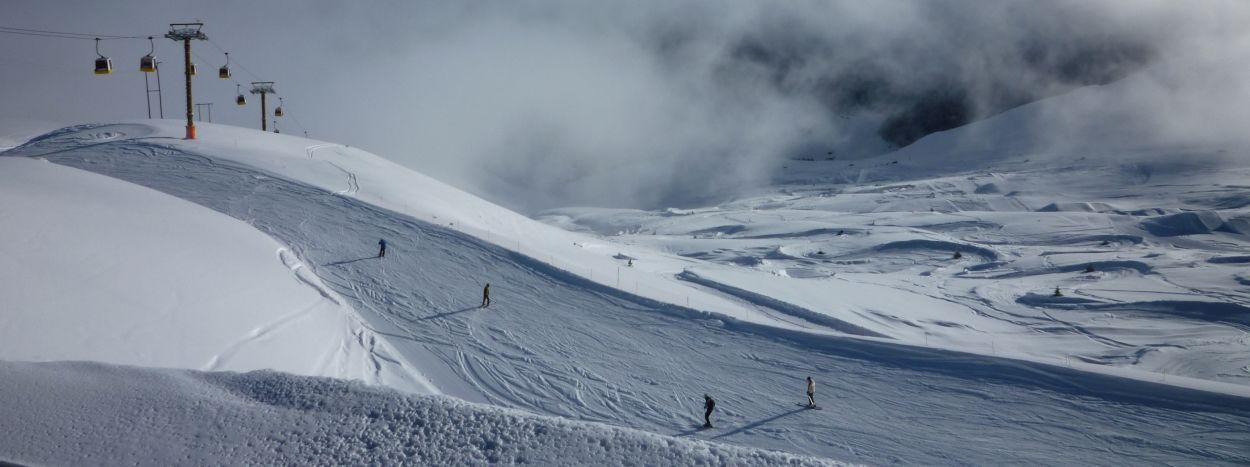 En sneklædt skibakke i Saalbach med et par skiløbere, der graciøst falder ned. Landskabet er dækket af nysne under en overskyet himmel, med skilifte til venstre og spor carving-mønstre på den uberørte overflade, der er indbegrebet af den ultimative skirejseoplevelse.